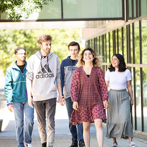 Five students laughing and walking down a sidewalk.