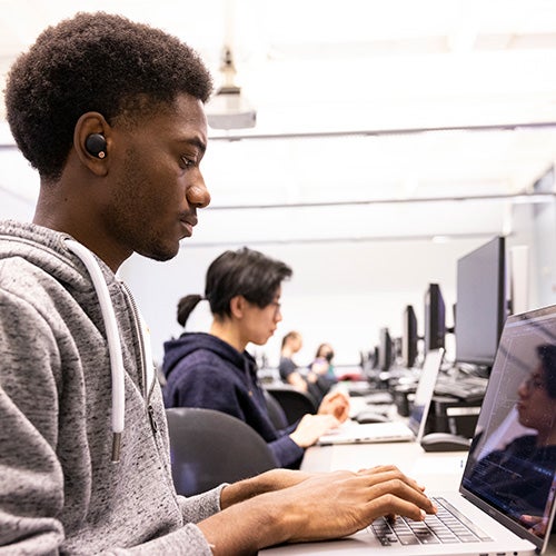 Young man sitting at desk, working on laptop computer.