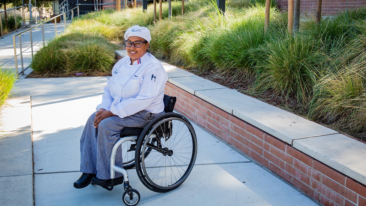 A student sits in a wheelchair and smiles for a picture.