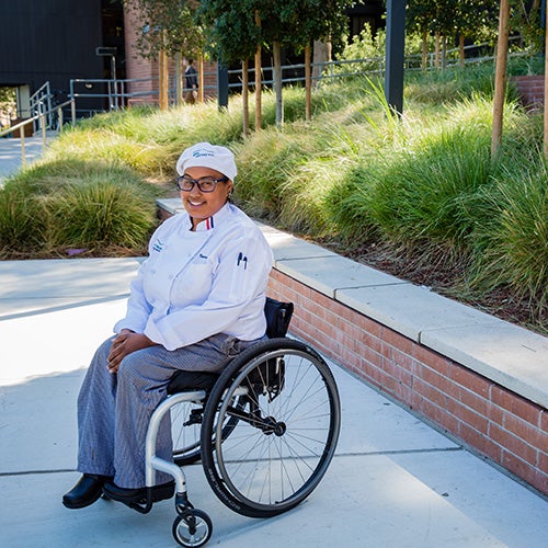 A student sits in a wheelchair and smiles for a picture.